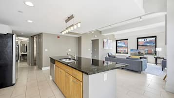 Een moderne keuken met een centraal eiland, een zithoek met een bank en uitzicht op gebouwen door grote ramen.