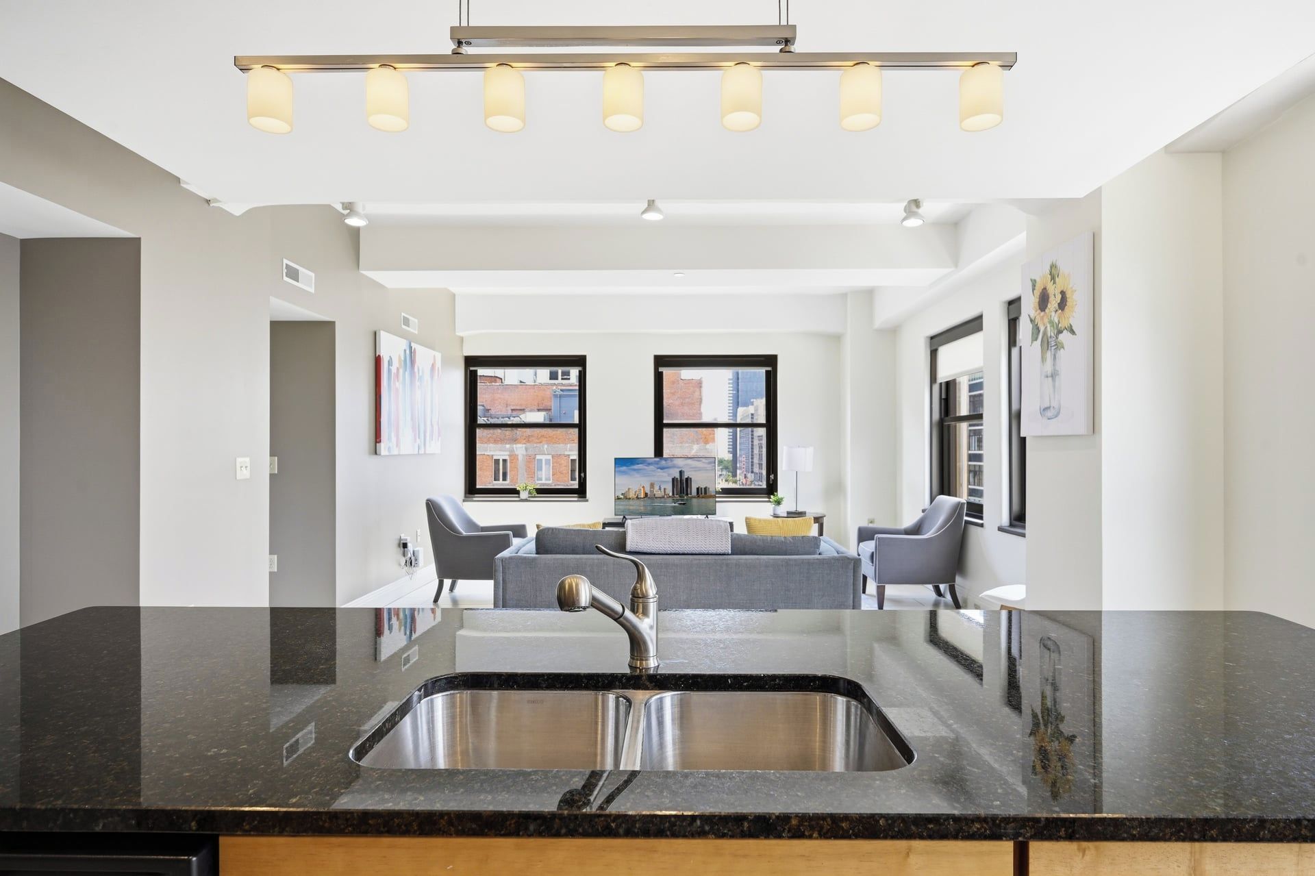A modern kitchen with a black countertop, stainless steel sink, and a pendant light fixture.