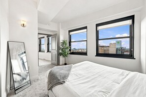 Habitación de hotel con una cama grande, un espejo y dos ventanas con vistas a la ciudad.