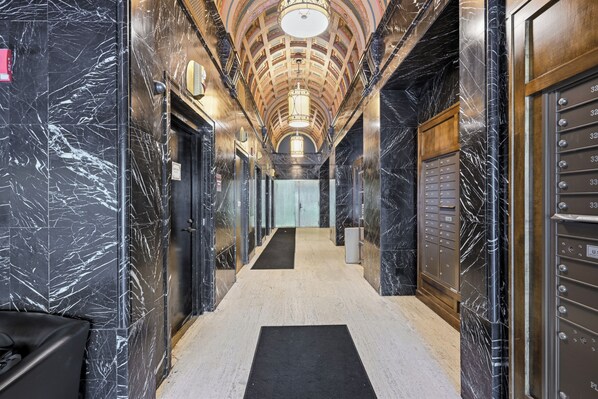 A marble-lined hallway with a black carpet, a ceiling with a circular design, and a row of lockers on the right.