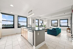 Um apartamento moderno com ilha na cozinha, área de jantar e sala de estar com sofá e vista para a cidade.