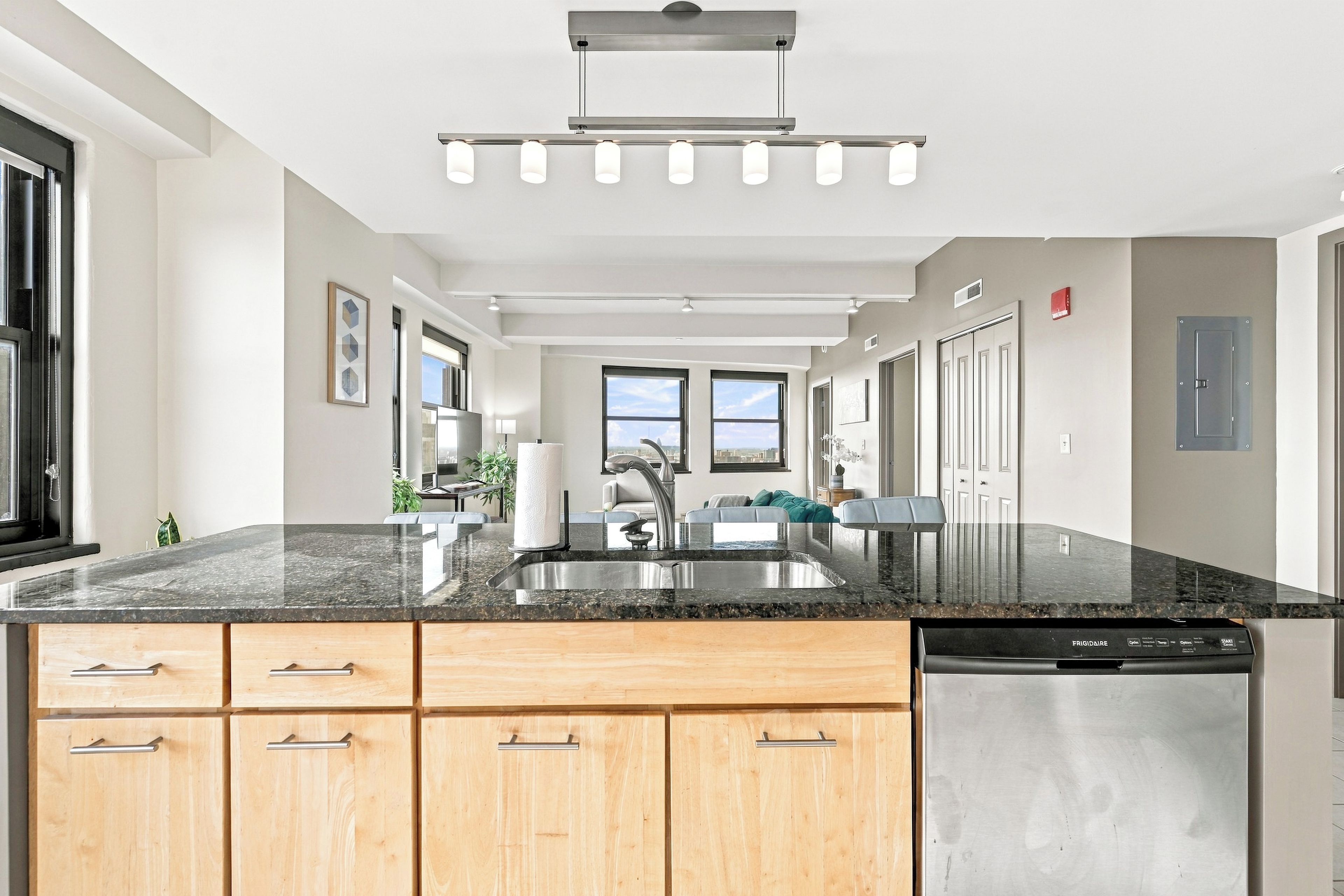 A modern kitchen with a granite countertop, wooden cabinets, a stainless steel dishwasher, and a built-in oven.