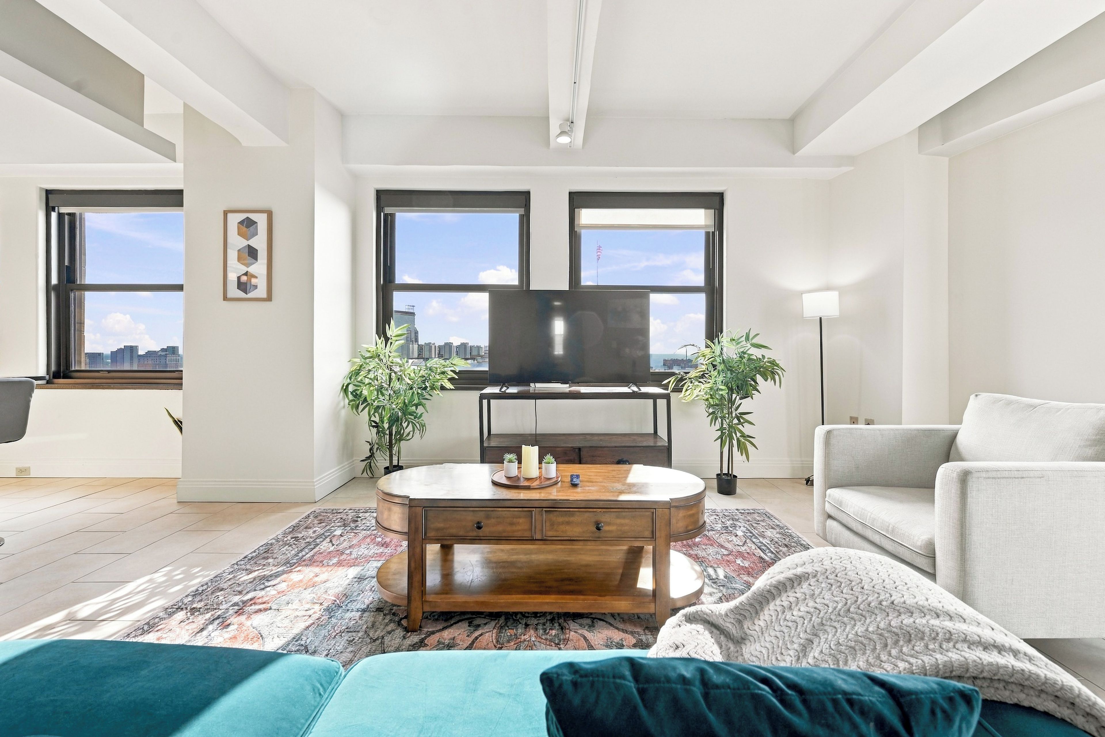Ein modernes Wohnzimmer mit Flachbildfernseher, Couchtisch, Sofa und zwei Topfpflanzen.