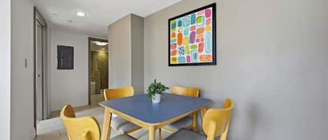 Un coin repas avec une table et des chaises, une plante en pot et un tableau abstrait aux couleurs vives accroché au mur.