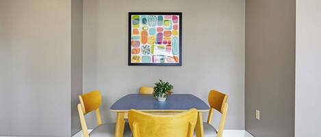 Comedor con una mesa y cuatro sillas, una obra de arte enmarcada en la pared y una planta en maceta sobre la mesa.