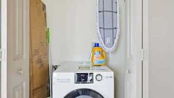 A laundry room with a front-loading washing machine, a drying rack, and a detergent bottle.