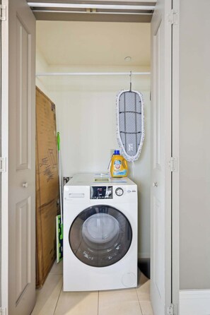 A laundry room with a front-loading washing machine, a drying rack, and a detergent bottle.