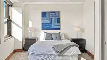 A bedroom with a bed, two bedside tables, a wall-mounted lamp, and a large abstract painting.