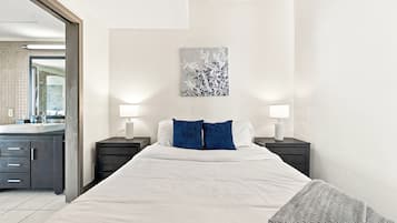 A hotel room with a large bed, two bedside tables with lamps, a wall-mounted artwork, and a view of the bathroom.
