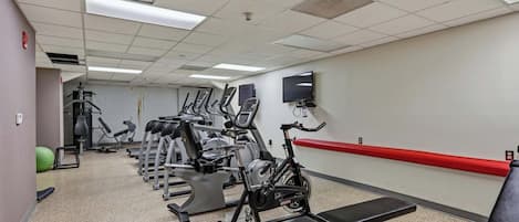 Un gimnasio con cintas de correr, bicicletas estáticas y una banca.