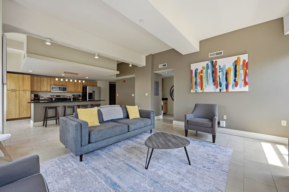 A modern living room with a grey sofa, a coffee table, and a kitchen in the background.