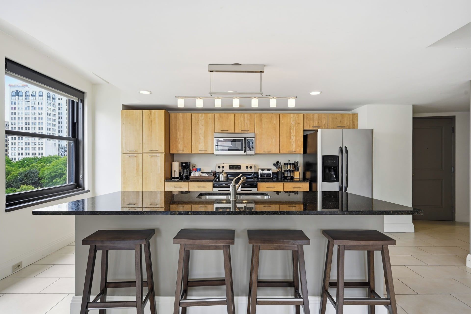 Une cuisine moderne avec des meubles en bois, un réfrigérateur en acier inoxydable, un four à micro-ondes et un grand îlot central doté de tabourets de bar.