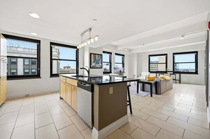 Uma cozinha moderna com ilha central, grandes janelas e vista para a paisagem urbana.