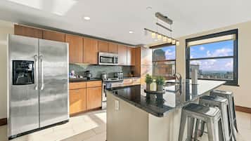 A modern kitchen with stainless steel appliances, wooden cabinets, a central island with stools, and a view of the city through large windows.