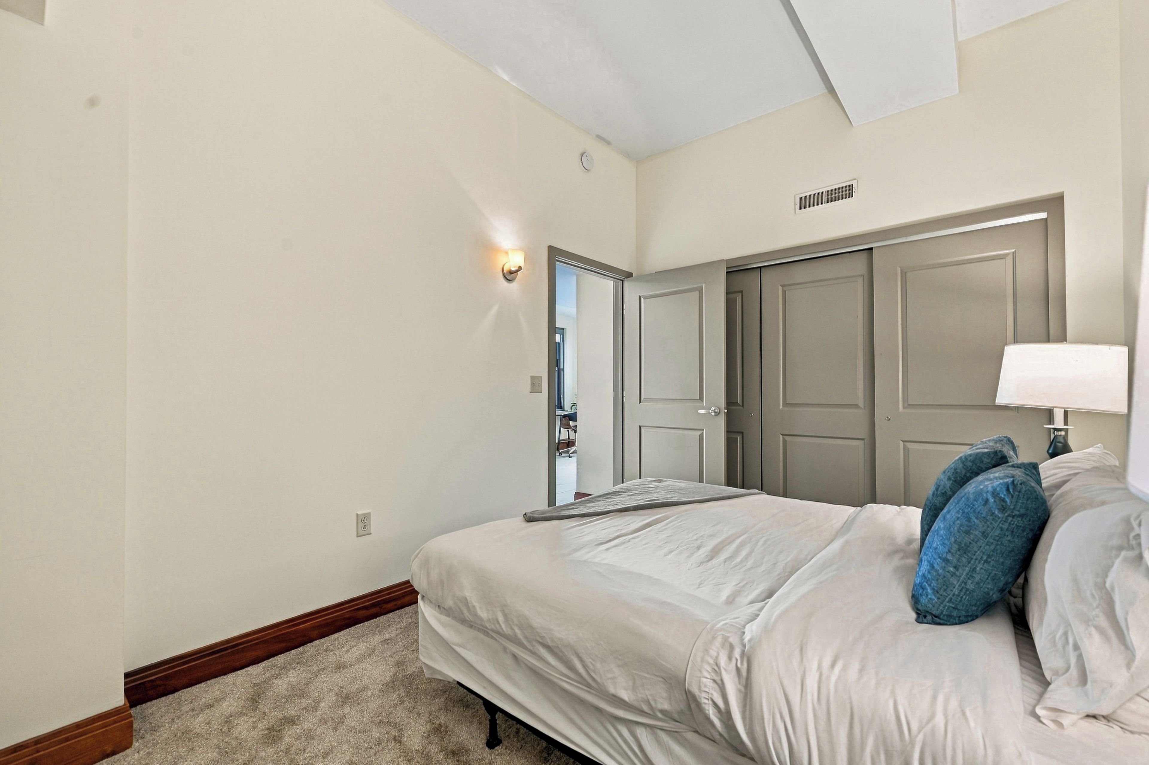 Un dormitorio con cama, mesita de noche, lámpara y puerta.