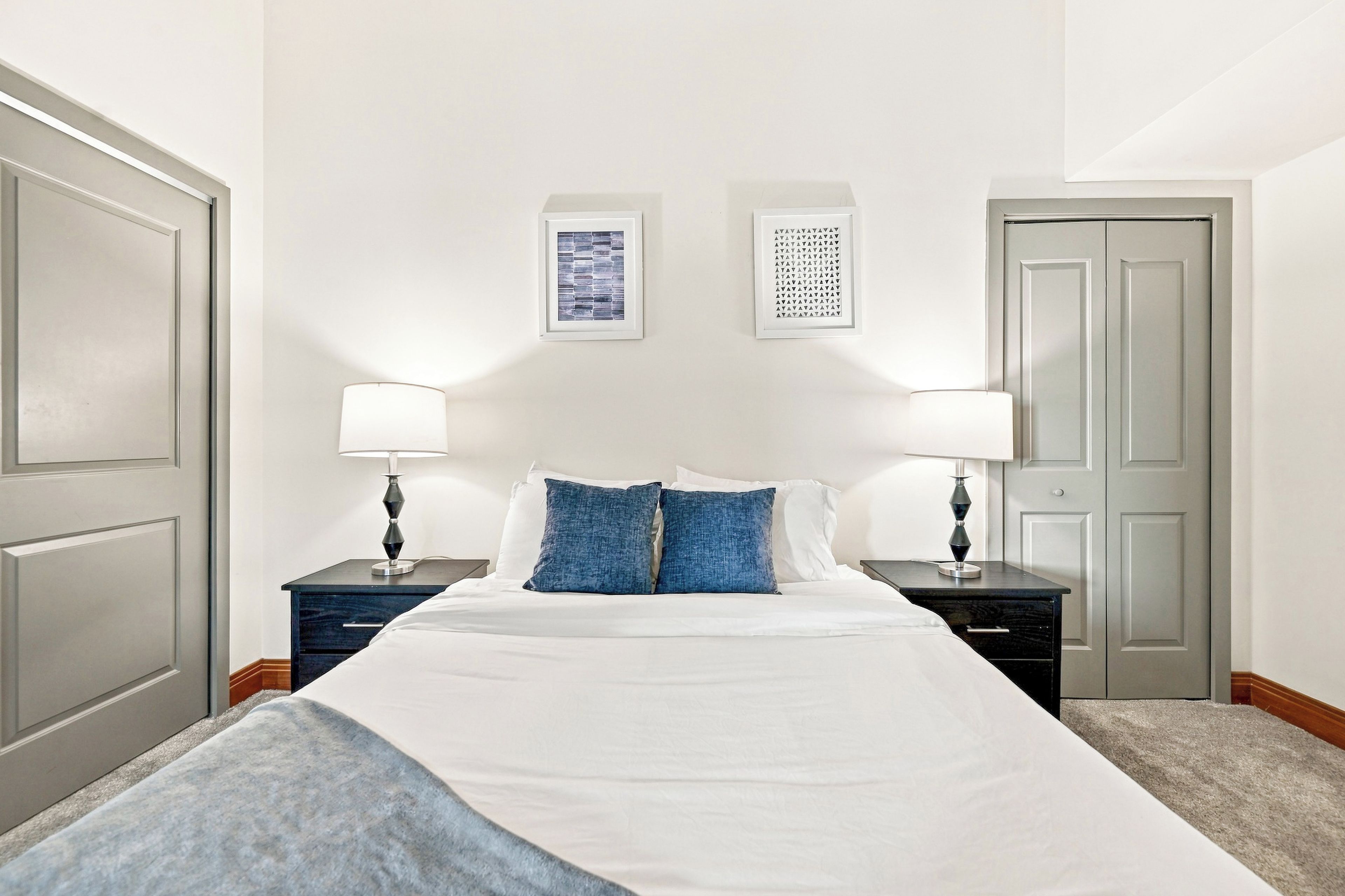 A hotel room with a bed, two nightstands, two lamps, a door, and two framed pictures on the wall.