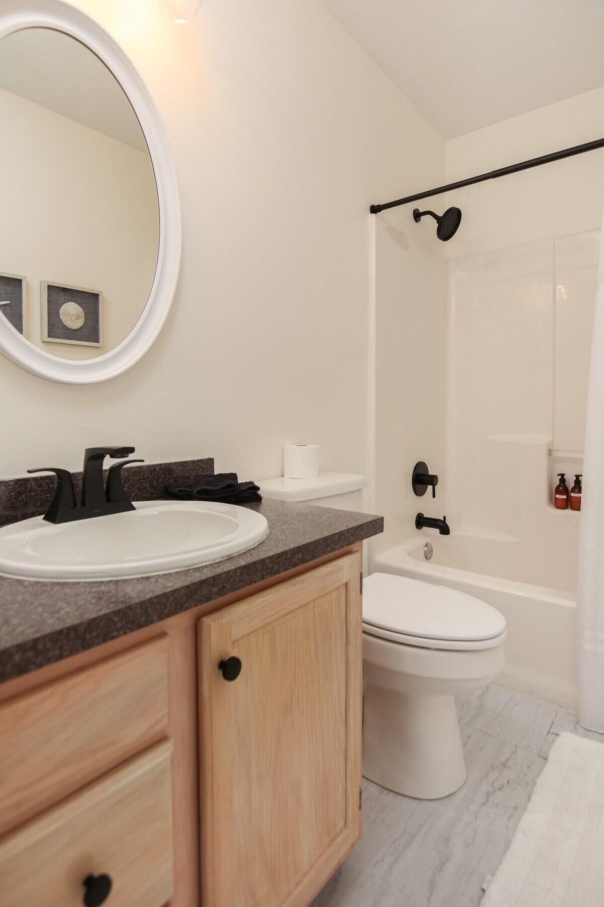 A modern bathroom with a round mirror, a sink, a toilet, and a shower area.