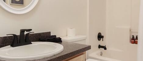 A modern bathroom with a round mirror, a sink, a toilet, and a shower area.