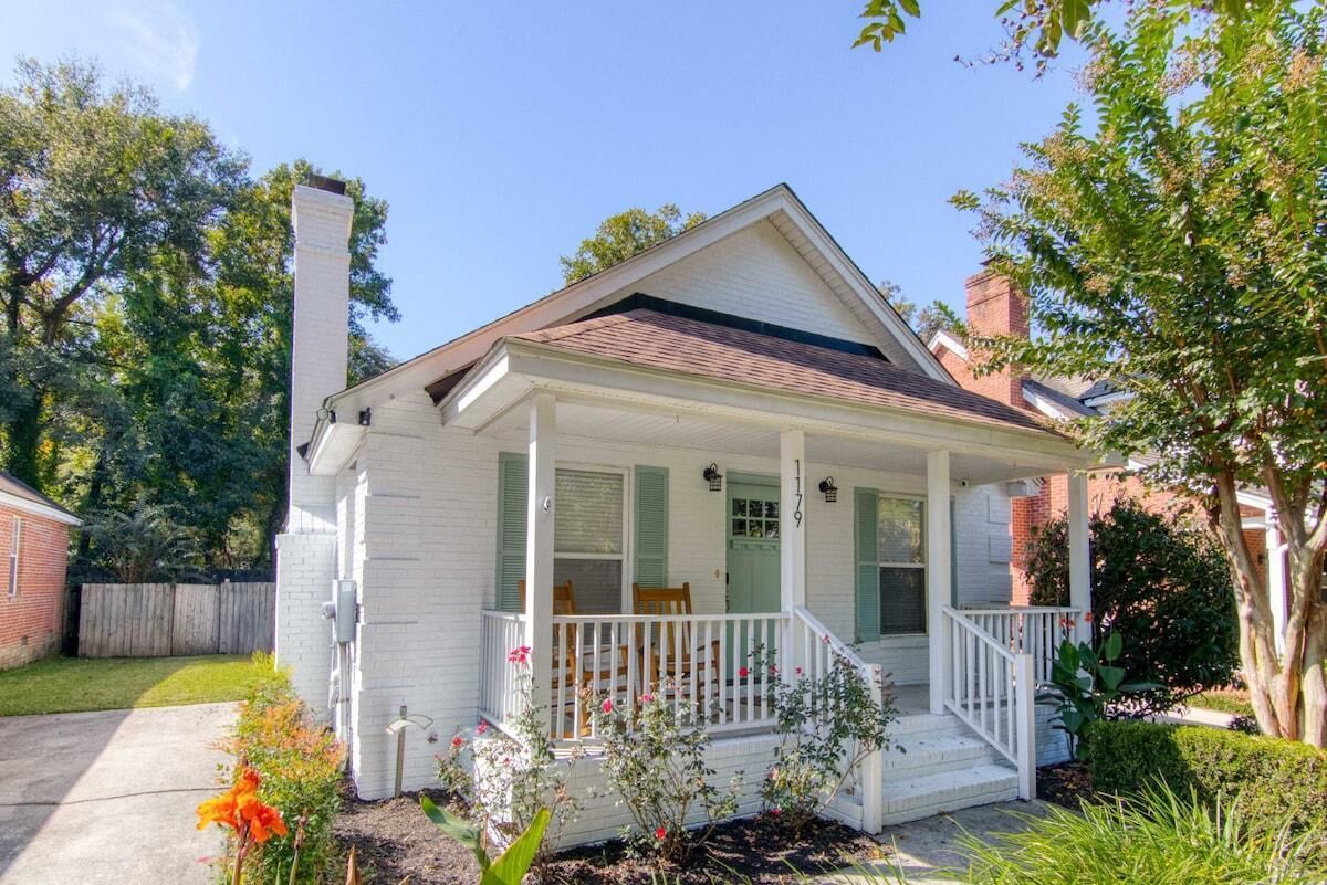 A single-story house with a front porch, a chimney, and a small garden with flowers.