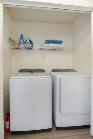 A laundry room with two white front-loading washing machines and a shelf above containing cleaning supplies. - Charleston Oasis With Hot Tub, Mins to Dtwn (Mount Pleasant)