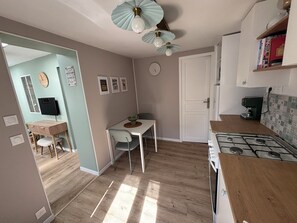 A compact kitchen with a gas stove, a dining table with chairs, a small white cabinet, and a ceiling fan. - 3-Star Vacation Rental “La maison de Doris” (Bihorel)