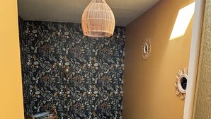 Ett litet sovrum med en enkel säng, en väggmonterad lampa och en tapet med mönster.