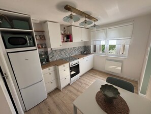 A modern kitchen with white cabinetry, a built-in microwave, a gas stove, and a window with blinds. - 3-Star Vacation Rental “La maison de Doris” (Bihorel)