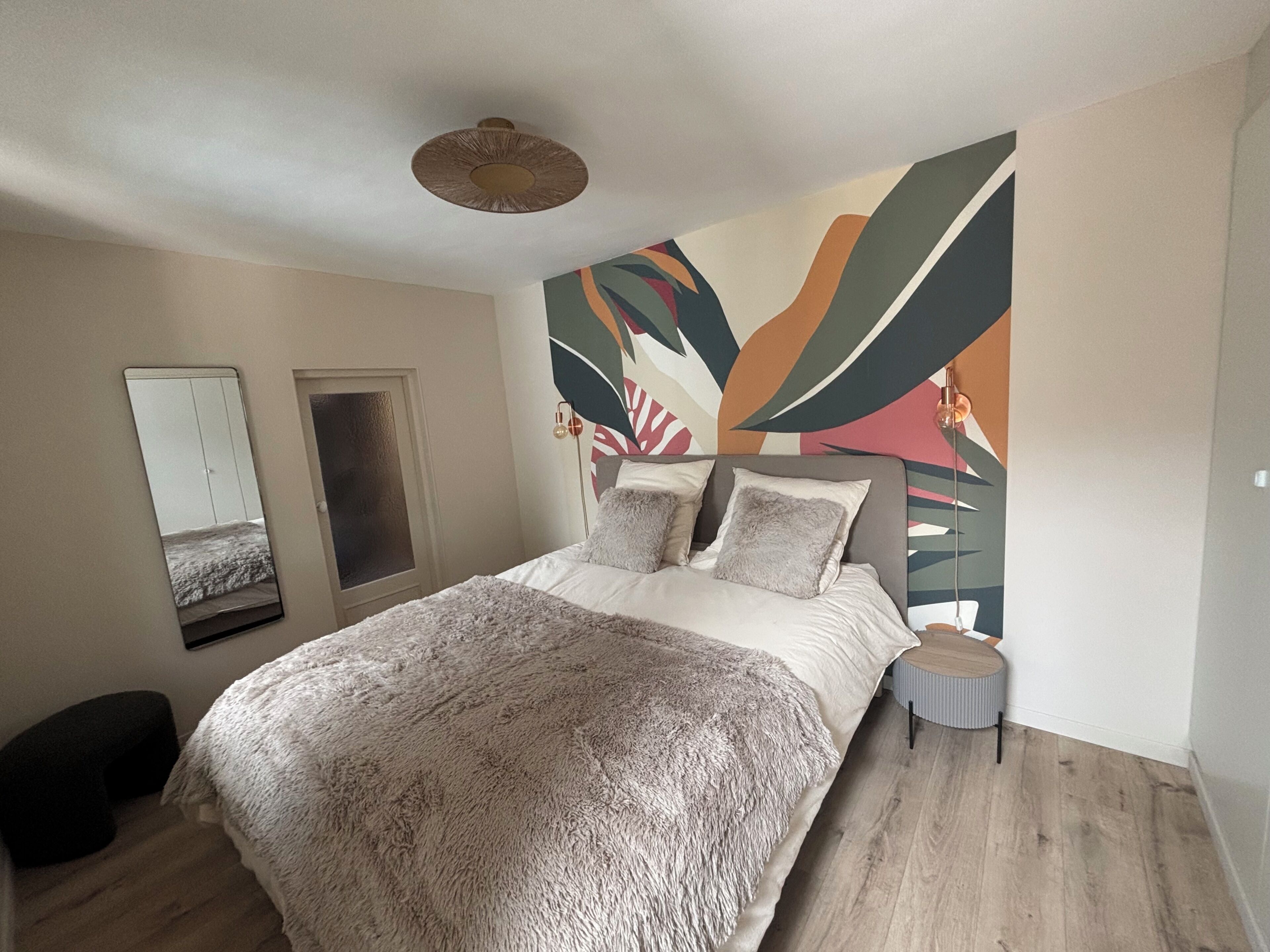 Une chambre à coucher avec un lit, un miroir, une porte et un mur orné d’œuvres d’art abstrait.