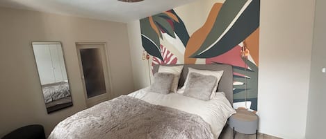 Un dormitorio con cama, espejo, puerta y una pared con arte abstracto.
