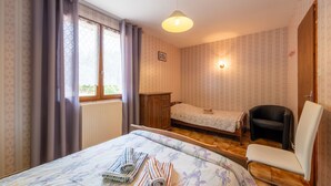 A room with a bed, a chair, a desk, and a window with curtains. - Apartment 'La Petite Caille - 5' with Wi-Fi (Plombières-les-Bains)