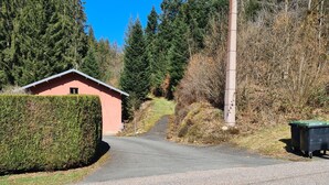 A gravel road leading to a small building with a pink facade, surrounded by dense greenery and a clear blue sky. - Apartment 'La Petite Caille - 5' with Wi-Fi (Plombières-les-Bains)