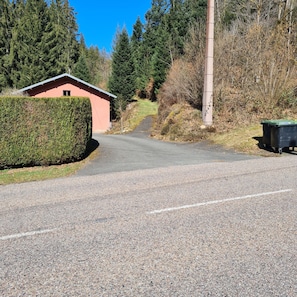 A gravel road leading to a small building with a red roof, surrounded by dense greenery and trees.