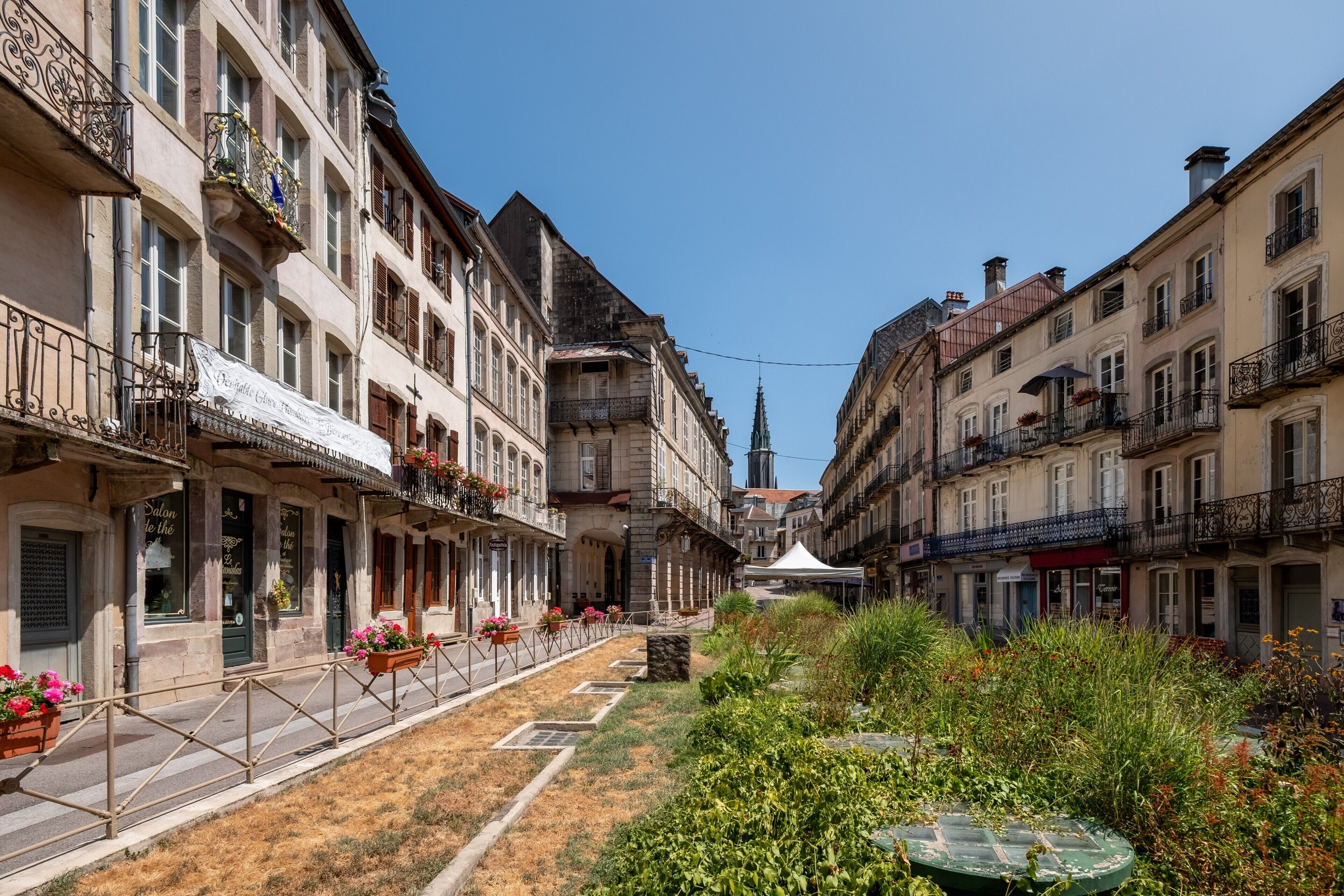 Une rue étroite bordée de bâtiments historiques, dont certains sont dotés de balcons et de jardinières.