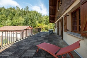 Ein Balkon mit Holzboden, einem roten Stuhl und einem Tisch mit Stühlen.