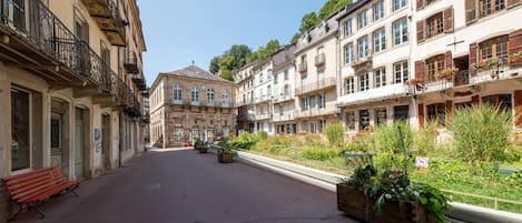 Une rue tranquille, bordée de bâtiments des deux côtés, avec un banc et des jardinières remplies de verdure.