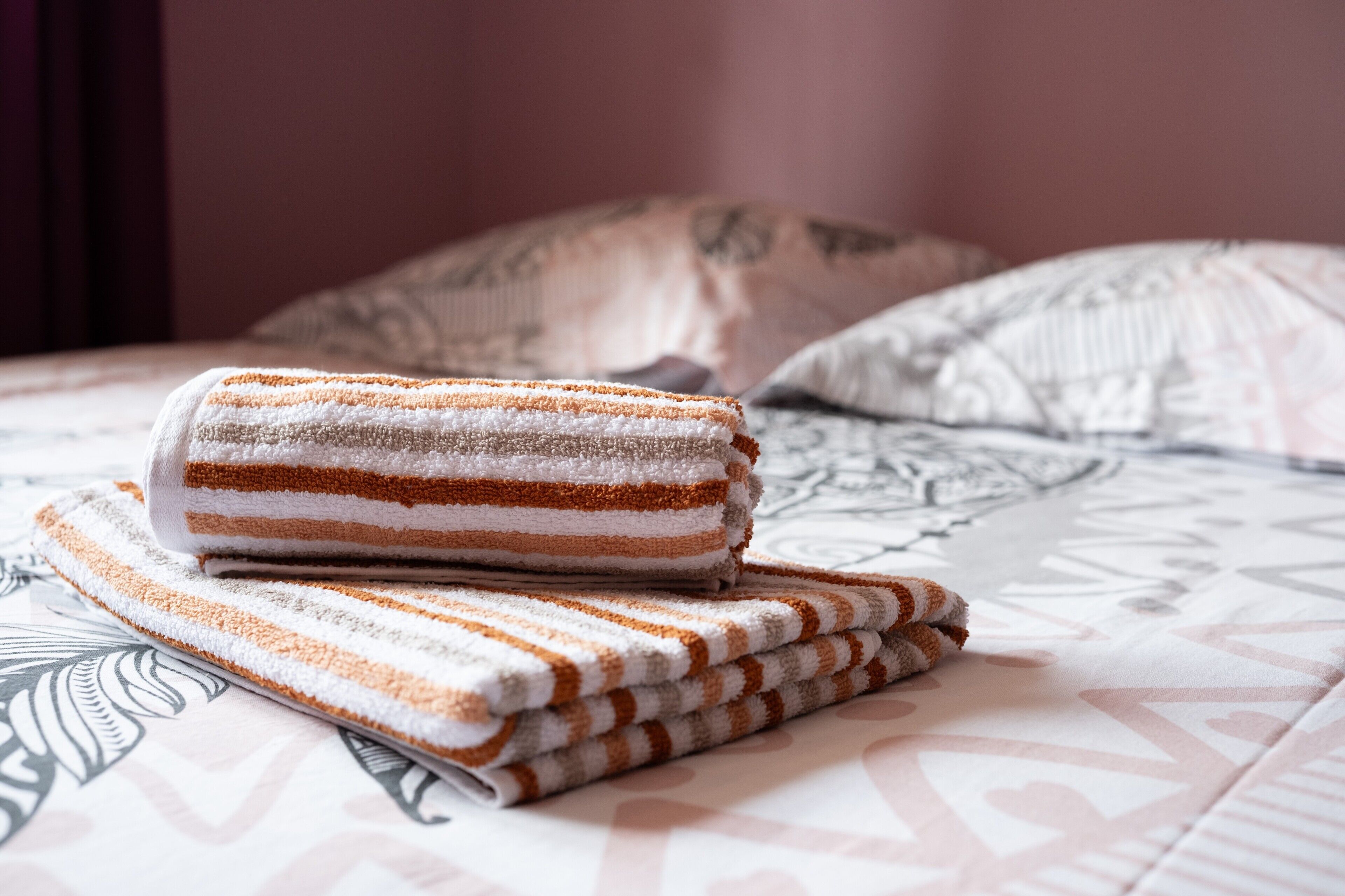 Una cama con una colcha estampada y una toalla rayada enrollada encima.