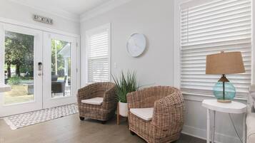 A room with two wicker chairs, a potted plant, a round wall clock, and a lamp on a small table.