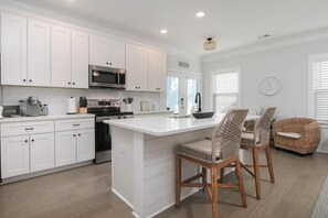 A modern kitchen with white cabinetry, a central island, and bar stools. - Southern Charming New Home-mins to Beach & DT (Mount Pleasant)