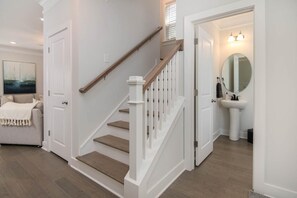 Una escalera con barandillas blancas y peldaños de madera que conduce a un baño con lavabo y espejo.