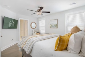 Une chambre à coucher comprenant un lit, un ventilateur de plafond, un téléviseur fixé au mur et une porte donnant sur une autre pièce.