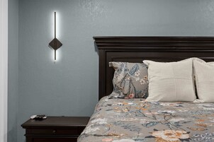 A bedroom with a bed, nightstand, and a wall-mounted light fixture.