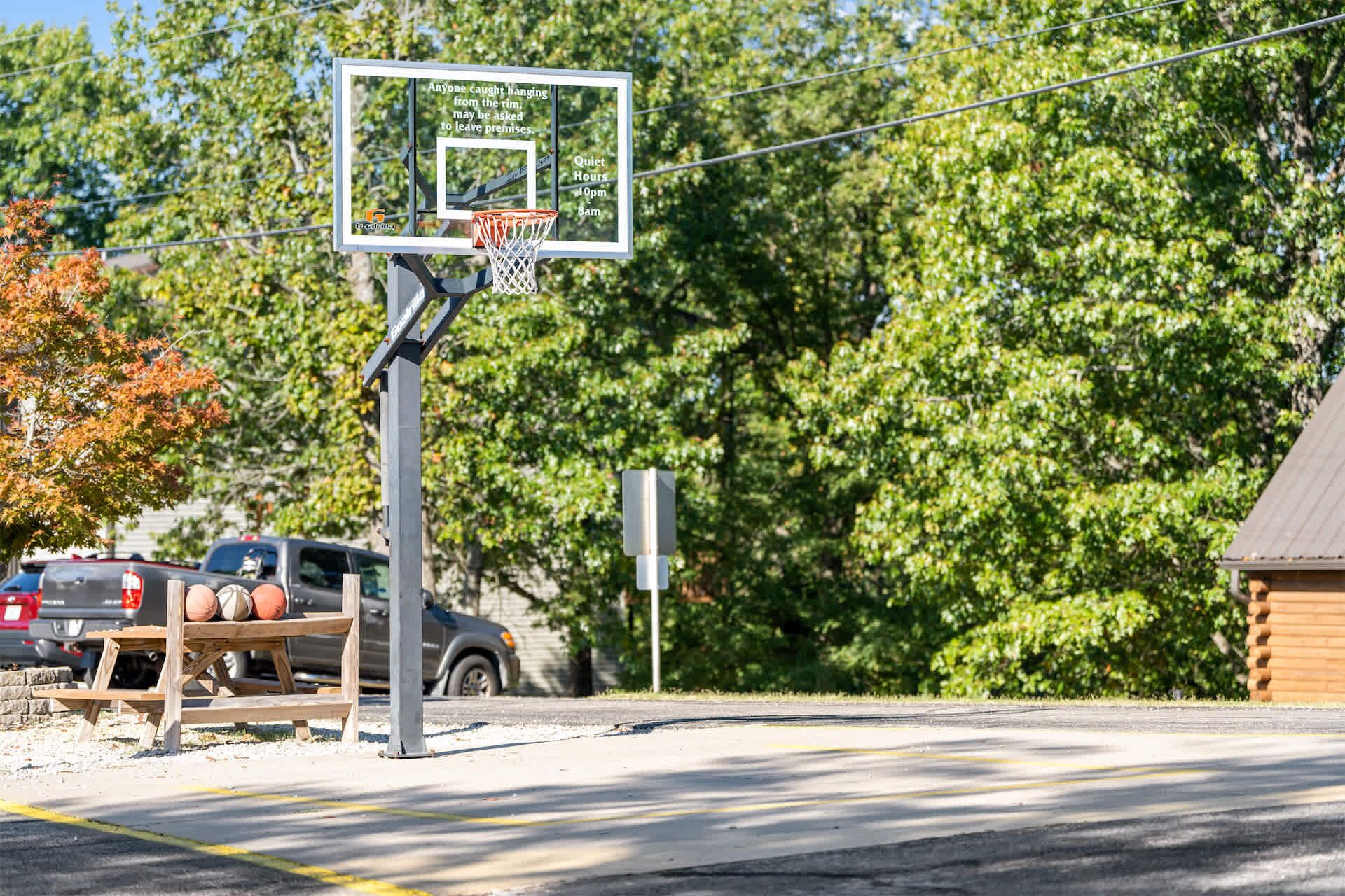 Ein Basketballkorb mit einem Warnschild, ein Picknicktisch mit Sportbällen und ein Gebäude im Hintergrund.