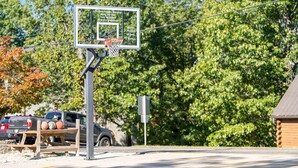 Ein Basketballkorb mit einem Warnschild, ein Picknicktisch mit Sportbällen und ein Gebäude im Hintergrund.