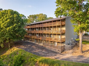 Un immeuble à plusieurs étages doté de balcons, d’un espace de stationnement et d’arbres.