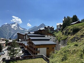 A mountain village with traditional wooden buildings, a road, and a view of snow-capped mountains. - Cabin studio with mountain view (Les Deux Alpes)