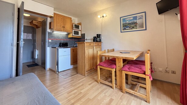 A compact kitchen with wooden cabinets, a microwave, and a coffee maker. There is a small dining table with two chairs. - Cabin studio with mountain view (Les Deux Alpes)