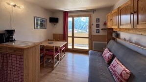 A compact kitchen with a dining table, wooden cabinets, a sofa, and a TV. - Cabin studio with mountain view (Les Deux Alpes)