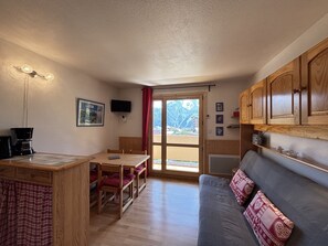 A compact kitchen with a dining table, wooden cabinets, a sofa, and a TV. - Cabin studio with mountain view (Les Deux Alpes)