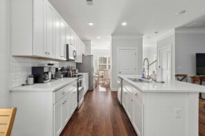 A modern kitchen with white cabinetry, a central island, and a wooden floor. - The Cozy Vibes-6 Beds-fenced in Backyard (Mount Pleasant)