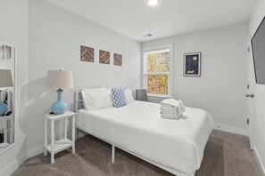A bedroom with a bed, a nightstand, a lamp, and a window with a view of trees. - The Cozy Vibes-6 Beds-fenced in Backyard (Mount Pleasant)
